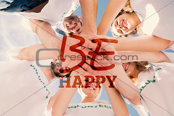 Composite image of happy volunteers with hands together against blue sky