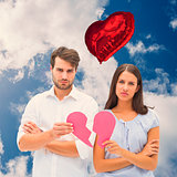 Composite image of upset couple holding two halves of broken heart