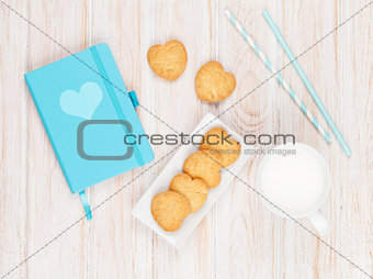 Cup of milk, heart shaped cookies and notepad