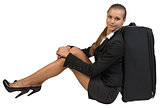 Businesswoman sitting next to side view suitcase, hugging her knees, looking at camera