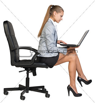 Businesswoman sitting on the edge of office chair, with laptop
