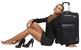 Businesswoman with her shoes off sitting hand resting on the floor, next to front view suitcase