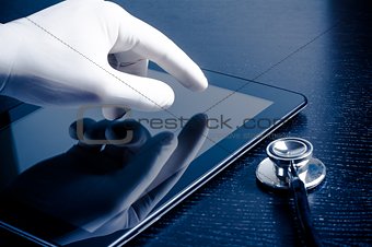 hand in medical glove touching modern digital tablet pc near stethoscope