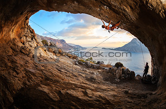 Young woman lead climbing in cave with beautiful view in background
