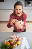 Happy young housewife putting money into piggy bank after shoppi