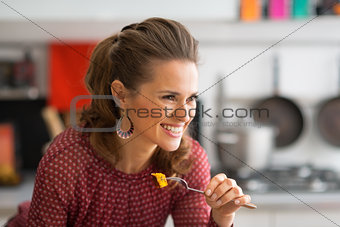 Portrait of happy young woman eating in kitchen