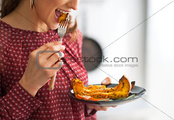 Closeup on young woman eating baked pumpkin in kitchen