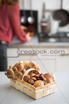 Closeup on basket with mushrooms on table and young housewife in