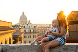 Mother and baby girl sitting on street overlooking rooftops of r