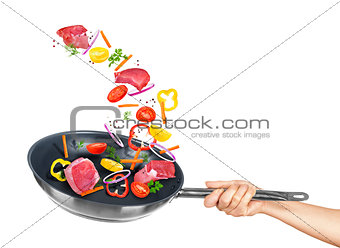 meat and mix vegetables fall into frying pan on a white backgrou