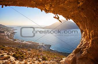 Male rock climber flexing his bicep while hanging on one arm at sunset. Climbing along roof in cave, Kalymnos, Greece