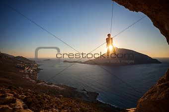 Rock climber hanging on rope while lead climbing at sunset, with Telendos island in background. Kalymnos island, Greece.