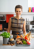 Portrait of happy young housewife with vegetables in kitchen