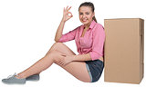 Woman sitting next to cardboard box, showing ok sign