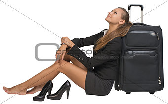 Businesswoman with her shoes off sitting next to front view suitcase
