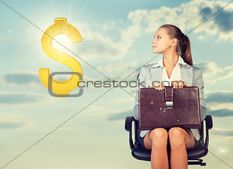 Businesswoman sitting on office chair, looking at dollar sign in the air