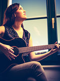 Beautiful woman playing guitar by the window