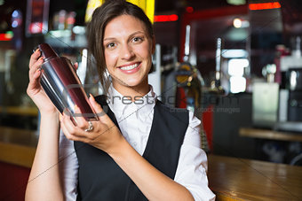 Happy barmaid smiling at camera making cocktail