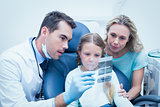 Dentist with assistant showing girl her mouth x-ray