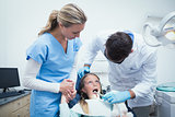 Dentist with assistant examining girls teeth