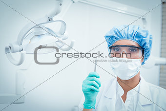 Dentist in surgical mask and safety glasses holding hook
