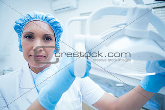 Serious female dentist adjusting light