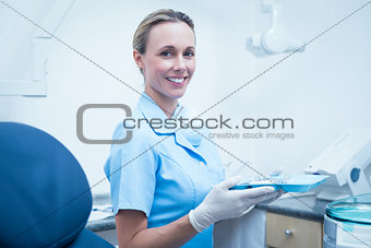 Female dentist in blue scrubs holding tray of tools