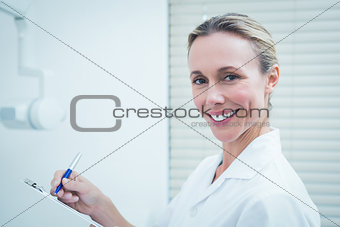 Smiling female dentist holding clipboard