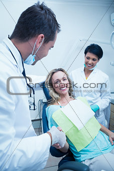 Dentist with assistant shaking hands with woman