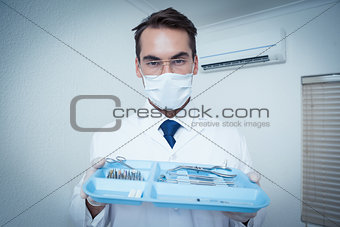 Male dentist in surgical mask holding tray of tools