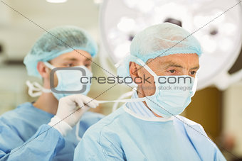 Young surgeon tying older surgeons mask
