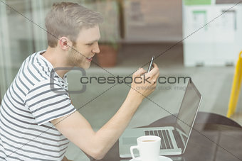 Smiling student using laptop and smartphone in cafe