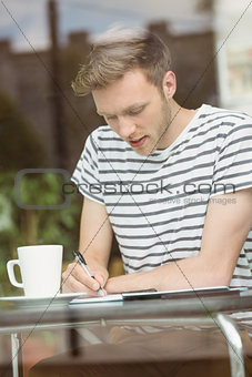 Smiling student sitting with a hot drink and writing on notepad