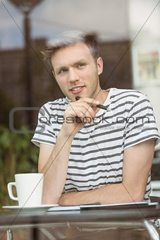 Thinking student sitting with a hot drink and holding a pen
