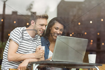 Smiling friends with a hot drink using laptop