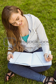 Smiling university student sitting and writing on notepad