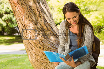 Smiling student sitting on trunk and reading book