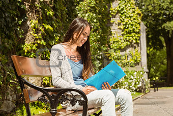 Smiling student sitting on bench and reading book