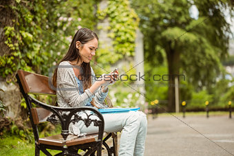 Smiling student sitting on bench text message on her mobile phone