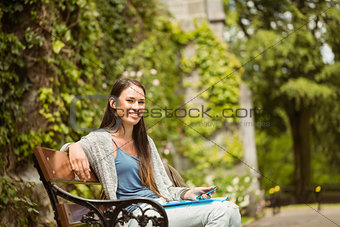 Smiling student sitting on bench holding her mobile phone