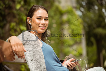 Smiling student sitting on bench listening music with mobile phone