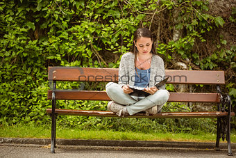 Student sitting on bench listening music with mobile phone and revising