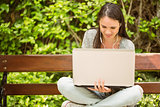 Smiling student sitting on bench listening music and using laptop