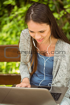 Smiling student sitting on bench listening music and using laptop