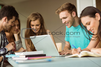 Smiling friends sitting studying and using laptop