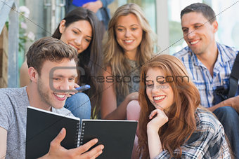 Happy students looking at book outside on campus
