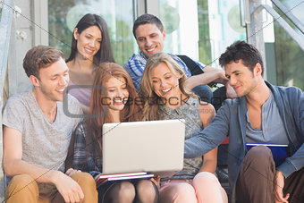 Happy students looking at laptop outside