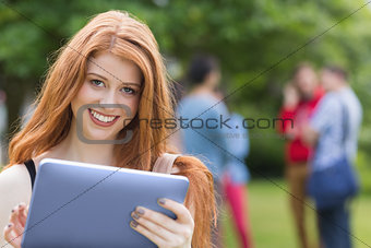 Pretty student smiling at camera using tablet pc