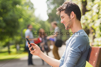 Handsome student sending a text outside
