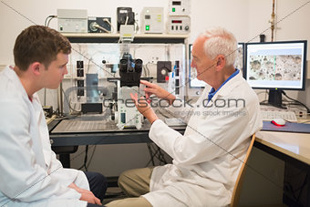 Biochemist using large microscope and computer with student